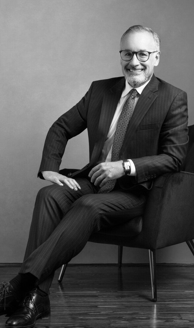 Businessman seated in chair, smiling in suit.