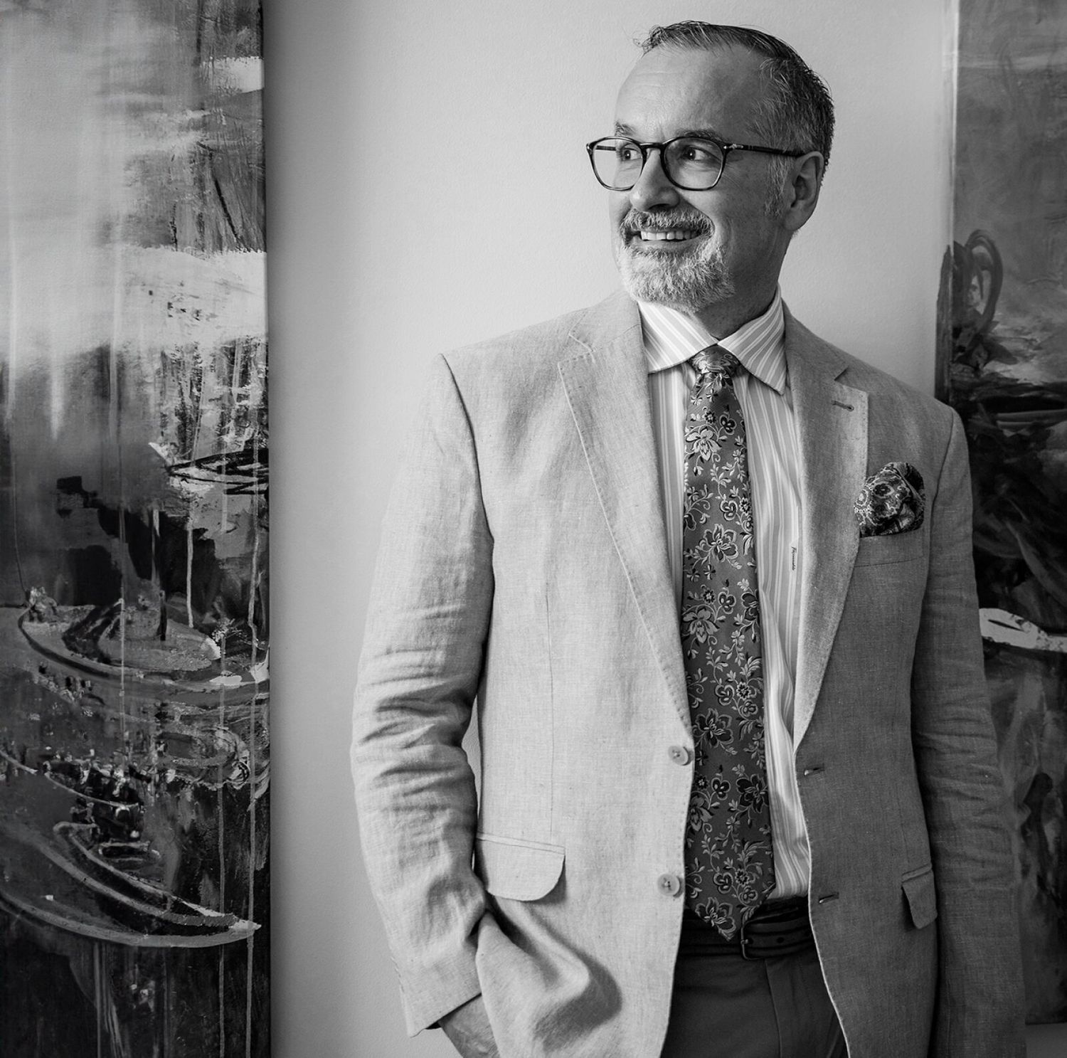 Man in suit smiling beside abstract artwork.