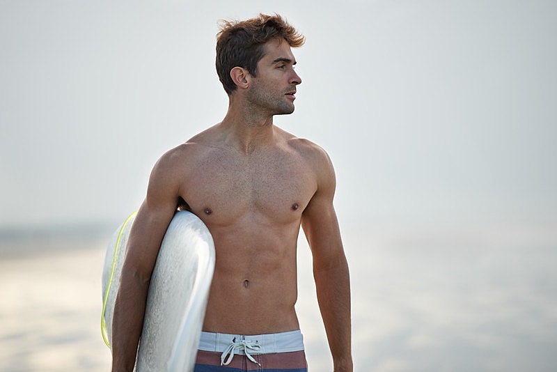 Shirtless man holding a surfboard at beach.