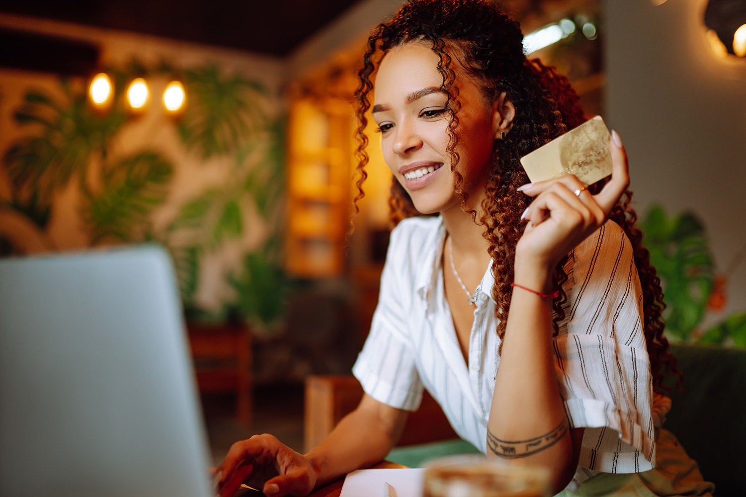 Woman using laptop, holding credit card, smiling.