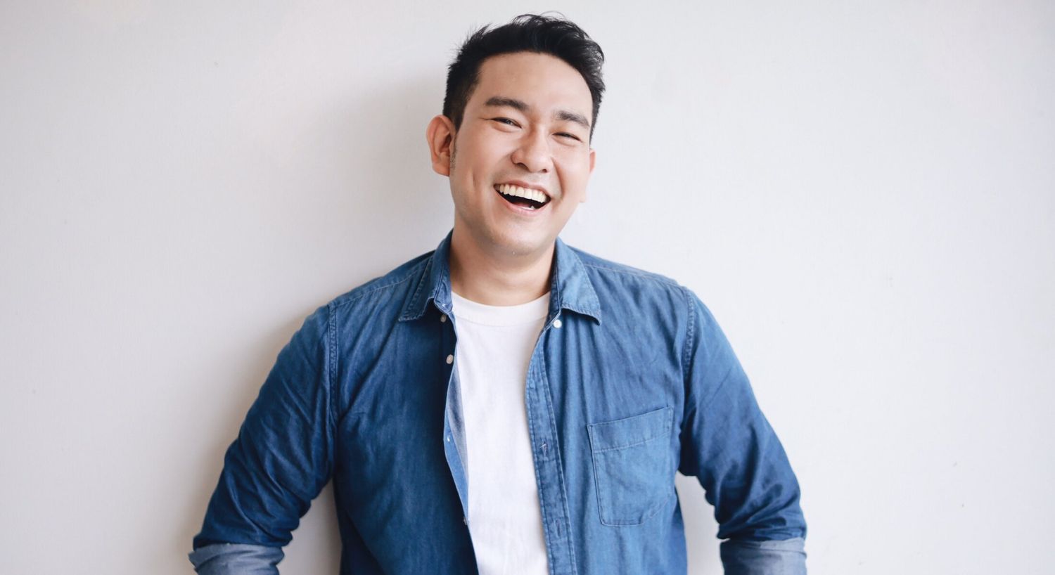Smiling man in denim shirt against white background.